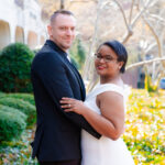 A man and woman hold their arms around each other while looking at the viewer and smiling