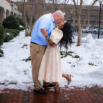a man and a woman kiss outside a courthouse as snow falls from the sky
